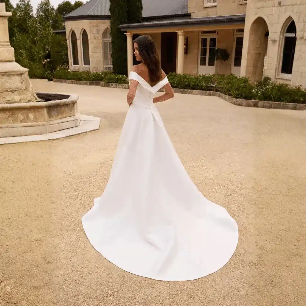 Bride in a flowing off-shoulder wedding dress standing in a courtyard.